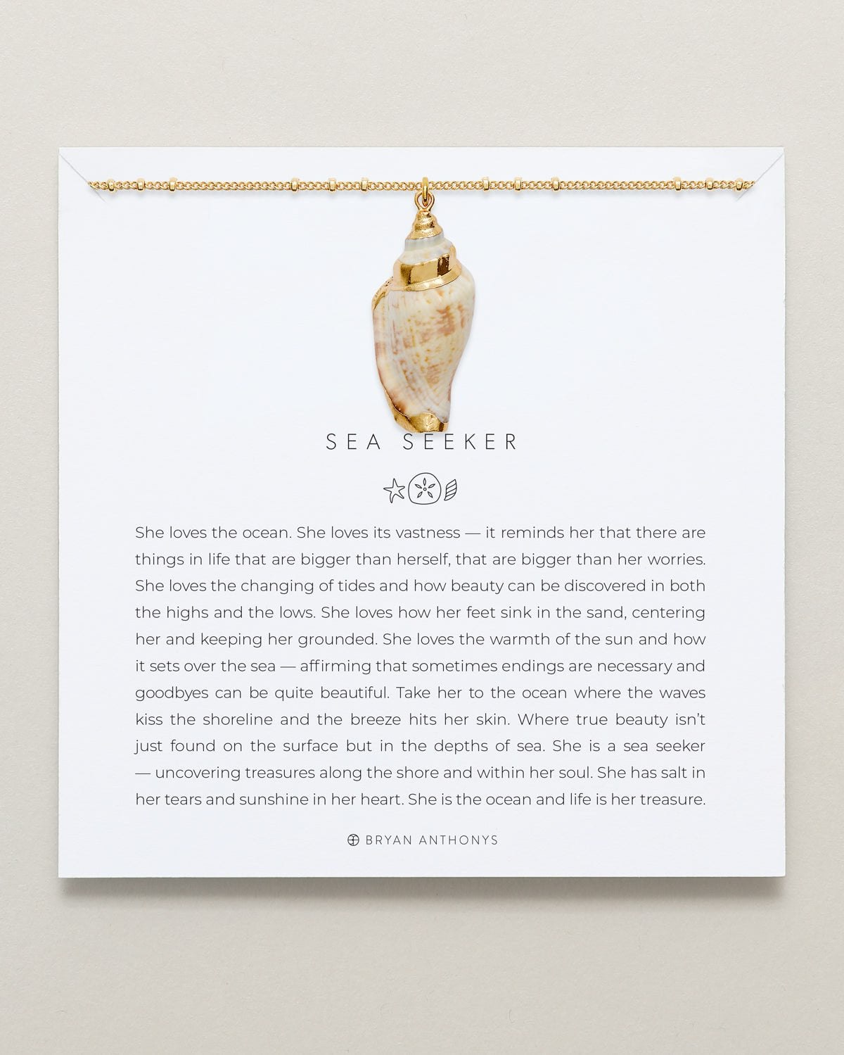 A gold ball chain necklace with a large, polished natural conch shell pendant hangs from the top edge of a white card. The card features the title 'SEA SEEKER' and a long message describing a person who loves the ocean.