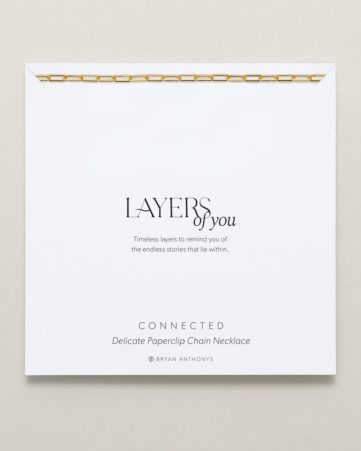 A delicate gold paperclip chain necklace is draped across the top edge of a white card. The card features the title 'LAYERS of you,' a short message about timeless layers.