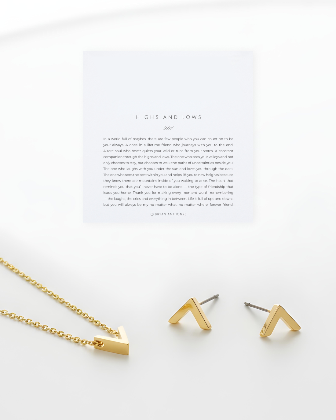A jewelry arrangement featuring two small, gold 'V' or arrow-shaped stud earrings and a gold chain necklace with a matching arrow pendant. Above them sits a white card titled 'HIGHS AND LOWS'.
