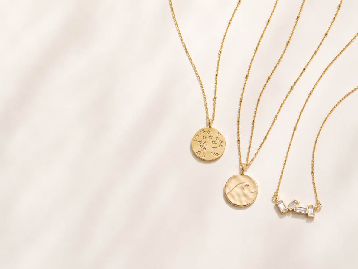 Three gold necklaces with different pendants on a light beige background