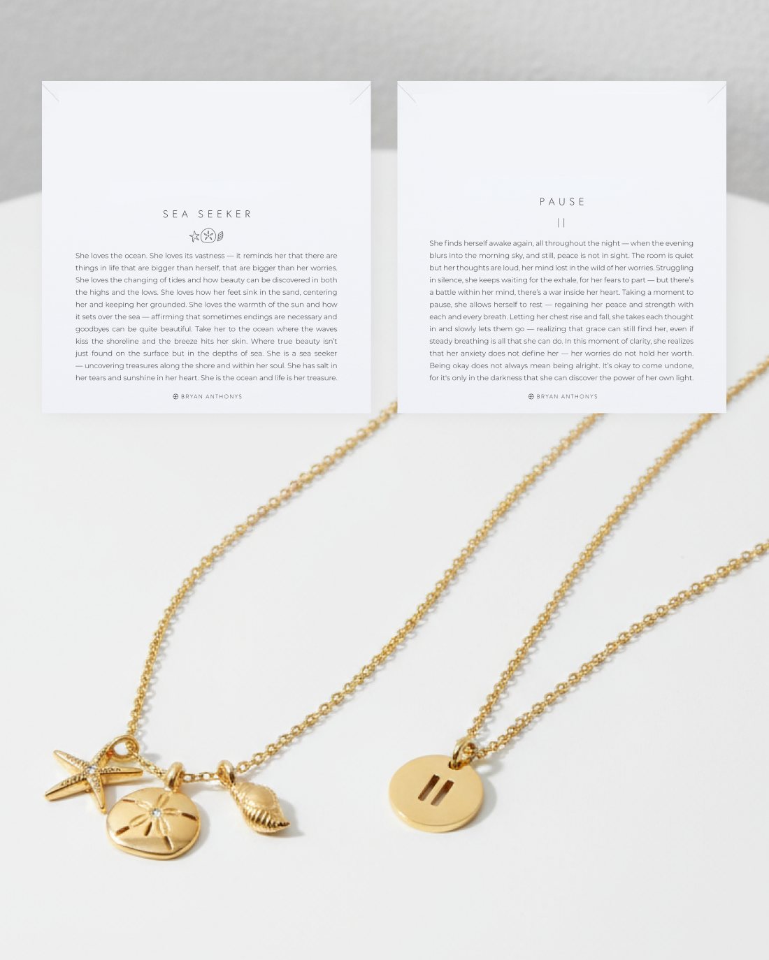 Two gold chain necklaces are laid out below their corresponding white cards. The left necklace features ocean-themed charms (starfish, sand dollar, and shell), sitting below a card titled 'SEA SEEKER.' The right necklace features a round pendant with a vertical double line (pause symbol), sitting below a card titled 'PAUSE.'